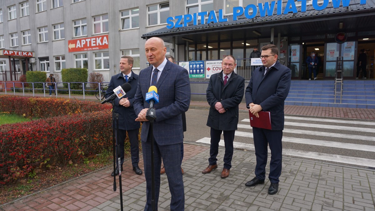 Mężczyzna stoi przed mikrofonem. Za nim czterech innych mężczyzn