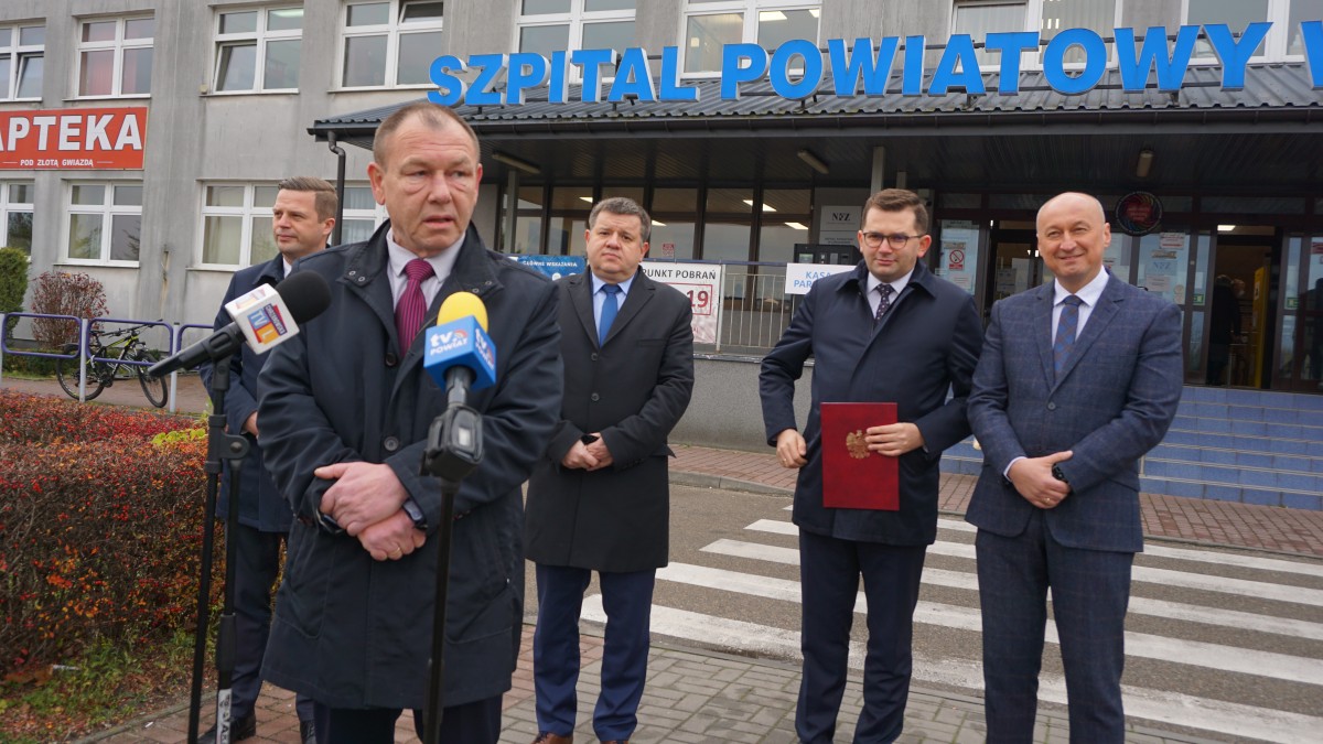 Mężczyzna stoi przed mikrofonem. Za nim czterech innych mężczyzn
