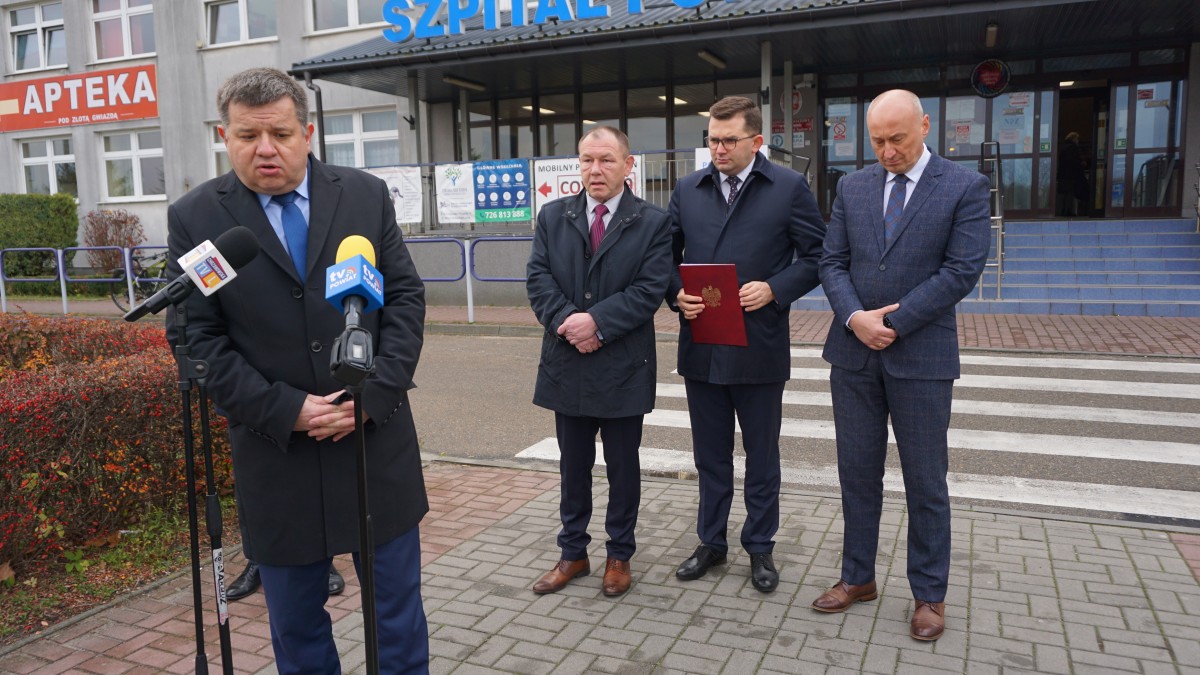 Mężczyzna stoi przed mikrofonem. Za nim czterech innych mężczyzn