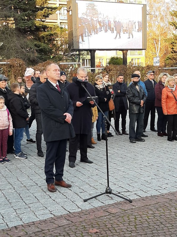 Mężczyzna stoi przed mikrofonem. Za nim tłum ludzi