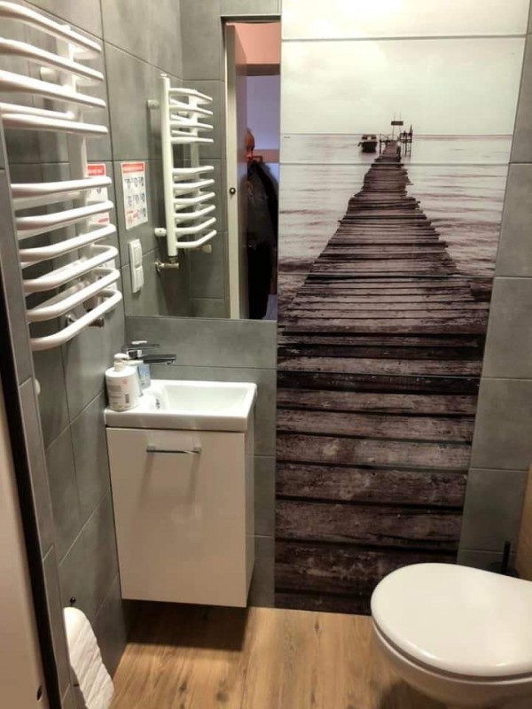 łazienka w wtz kaloryfew po lewej i umywalka z szafką - białe, ścianka z widokiem kładki i wody, opo prawej wc białe