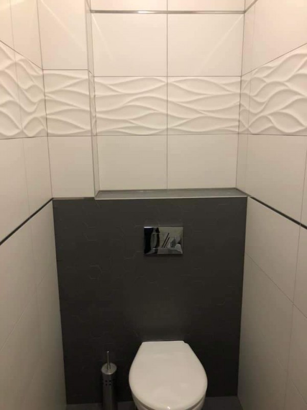 łazienka w wtz- zdjęcie wc - białe sciany z kafelek, poniżej szarek fafle (obudowa wc) oraz wc, obok wc szczotka do wc strebrna