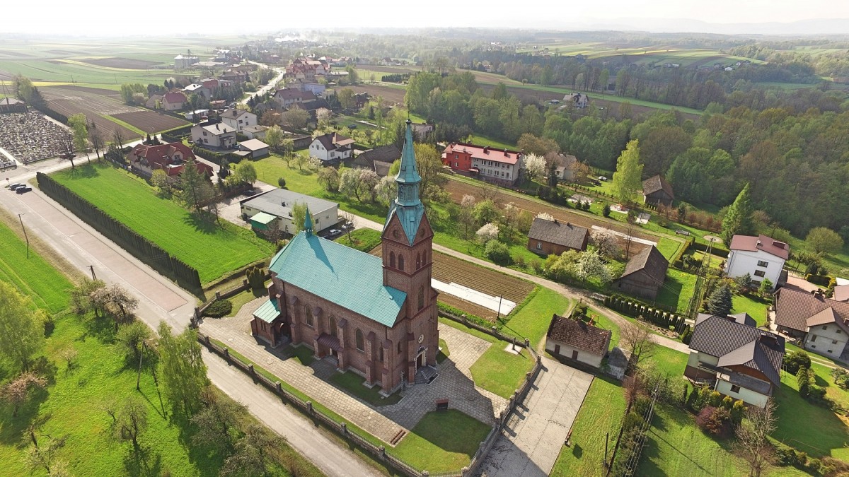 widko na kosciół z lotu ptaka kościół strzlisty wokół zabudowania - domy dużo terenów zielonych trawa oraz drzewa