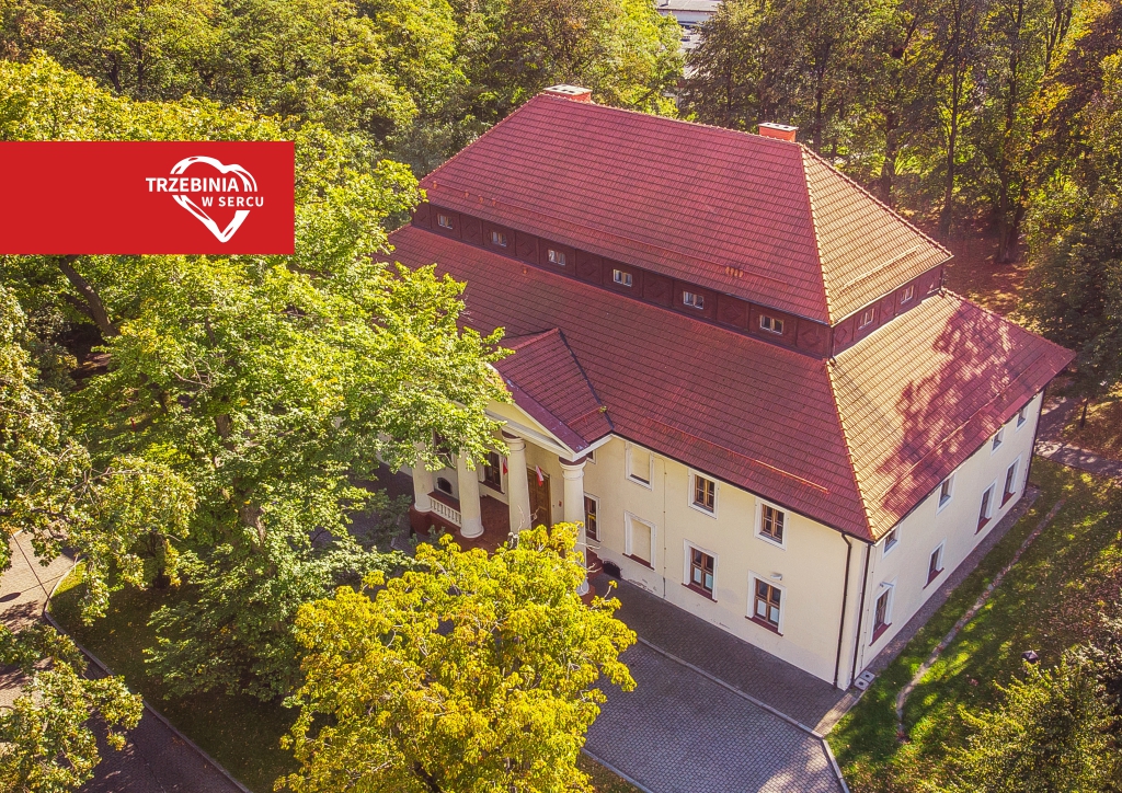 Biały budynek z pomarańczowym dachem wśród drzew, zdjęcie z lotu ptaka.