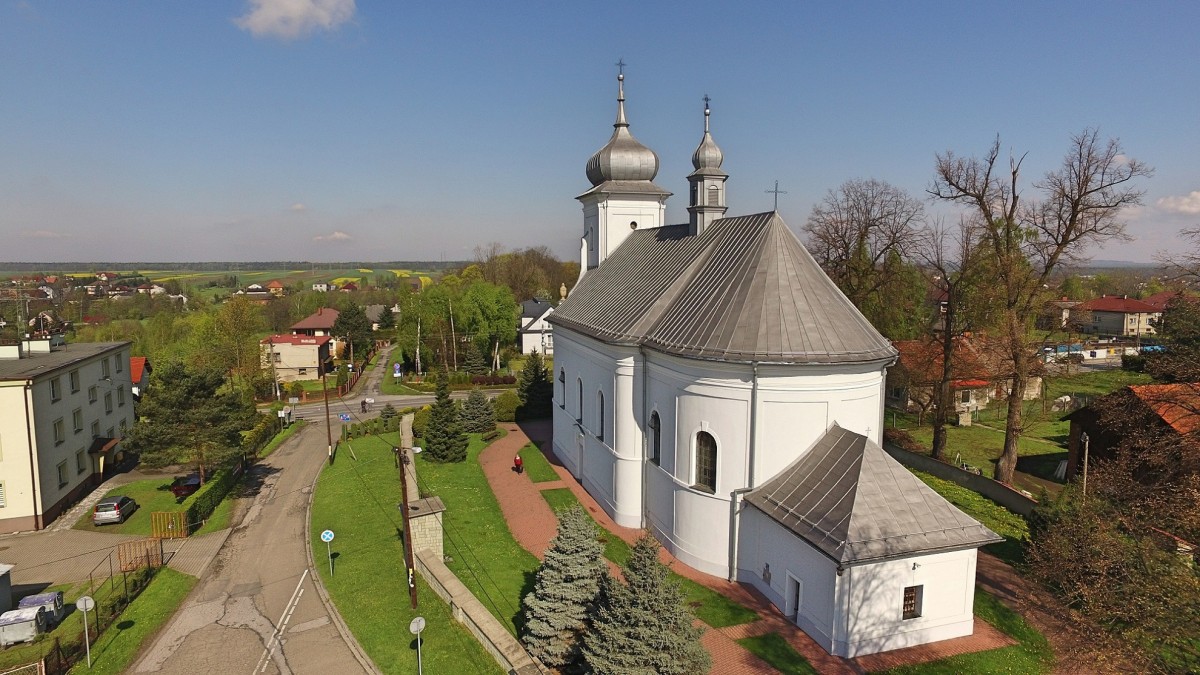 Kościół wymalowany na biało w otoczeniu zabudowań mieszkalnych i drzew.