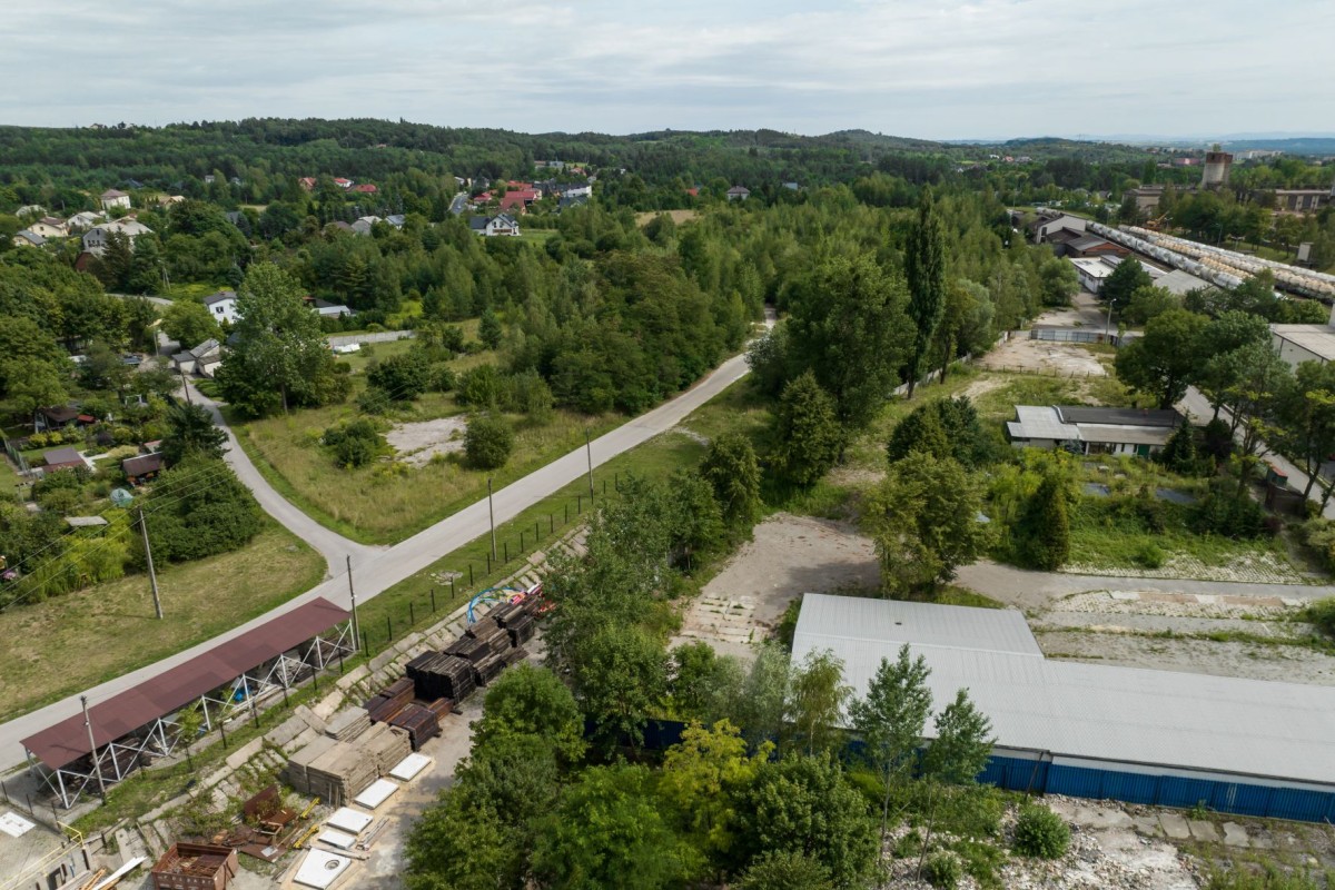 widok z lotu ptaka na działkę  wokół zieleń trawa i drzewa, wokół domy mieszkalne, budynki przemysłowe