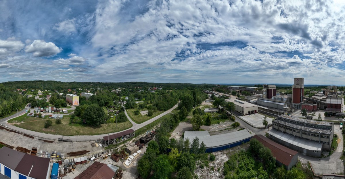 widok z lotu ptaka na działkę  wokół zieleń trawa i drzewa, wokół domy mieszkalne, budynki przemysłowe, droga asfaltowa