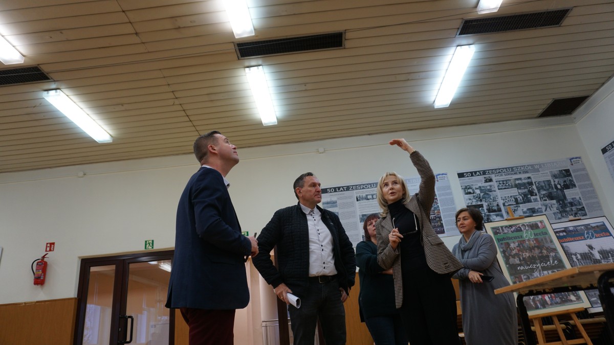 Grupa ludzi w kółku. Kobieta wskazuje na sufit 