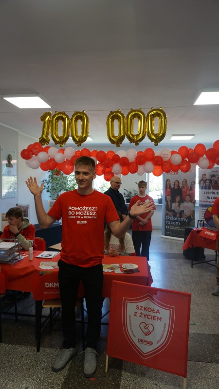 Zdjęcie ucznia z odnisionymi rękoma. Nad nim balony ułożone w liczbę 100 000. W tyle inne balony i uczniowie.