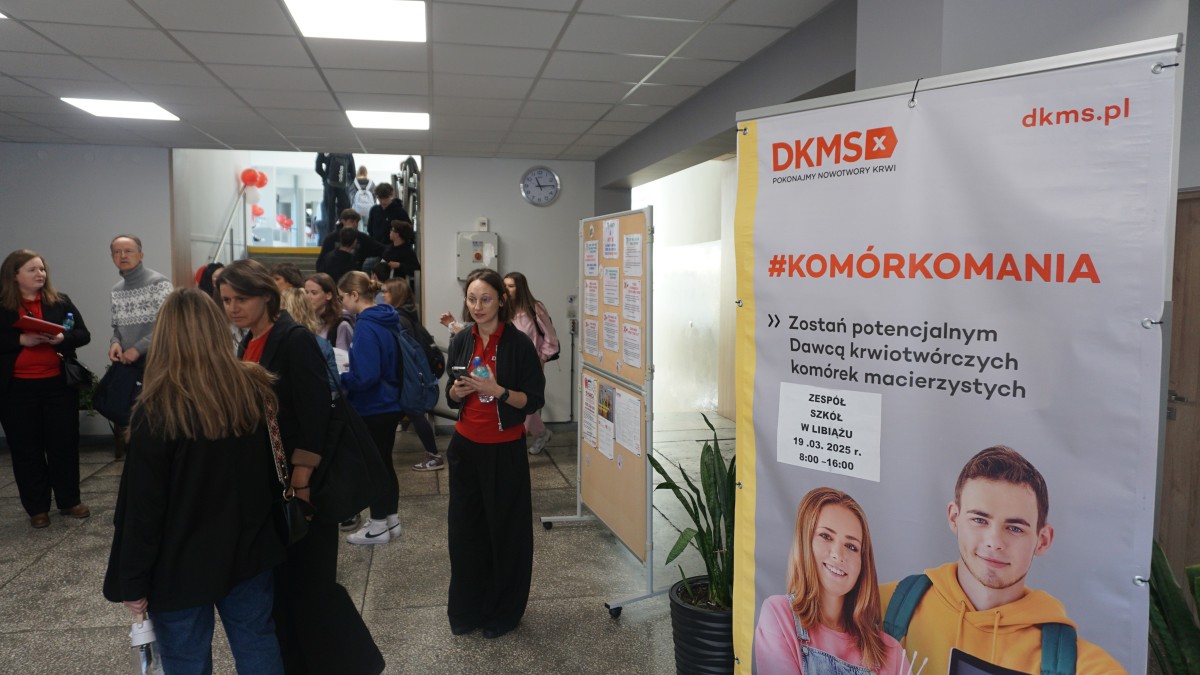 Zdjęcie baneru promującego wydarzenie. W tyle uczniowie i wolontariusze. 