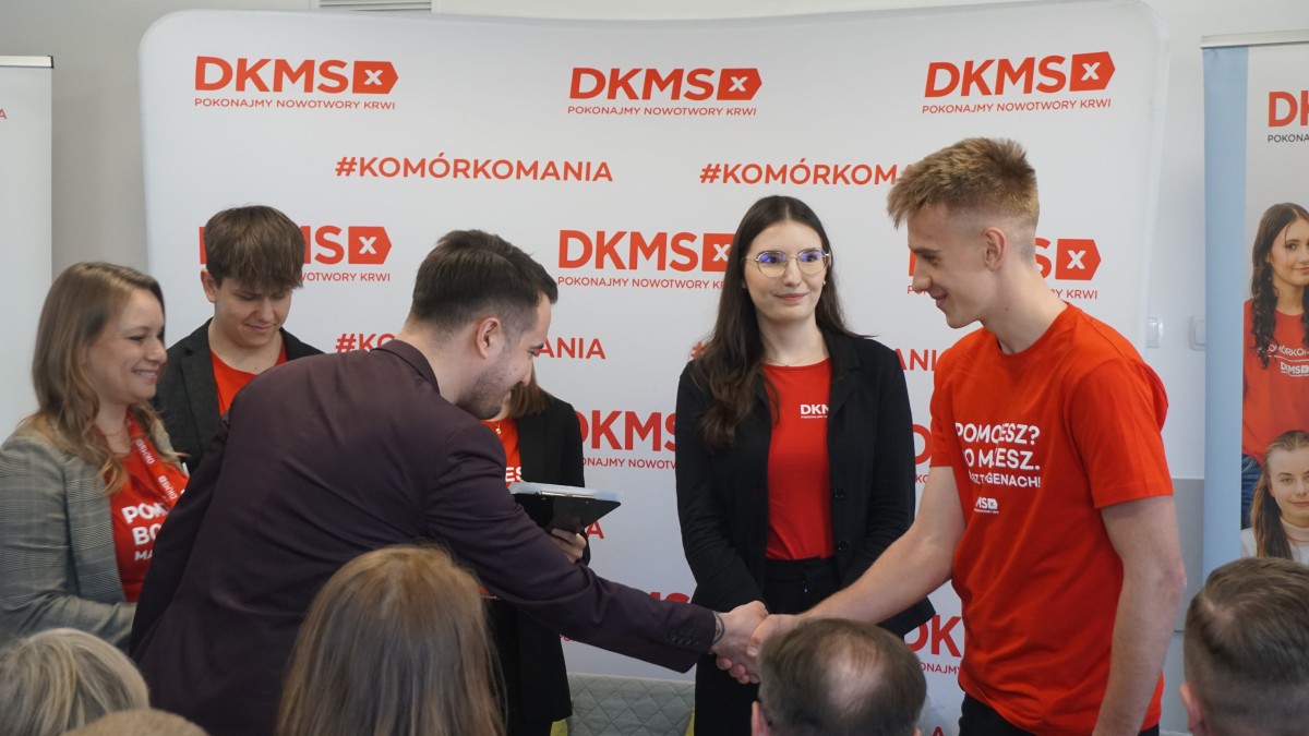 Zdjęcie 6 młodych osób. Dwaj mężczyni podaja sobie dłonie. 
