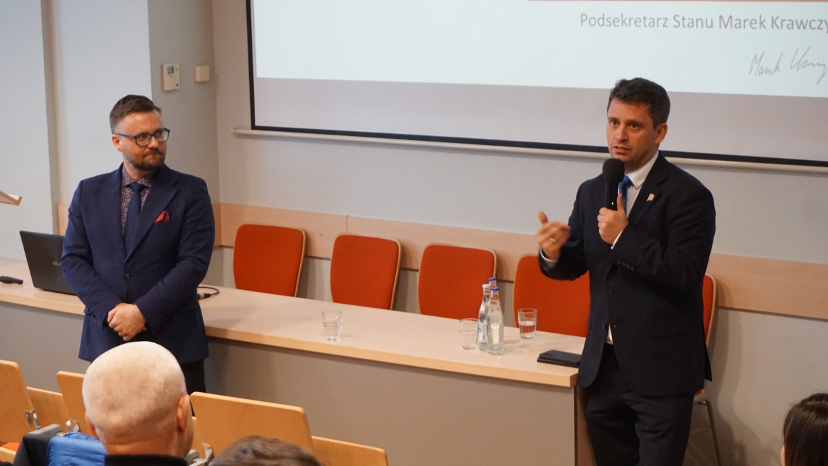Zdjęcie dwójki osób stojących i przemawiających.