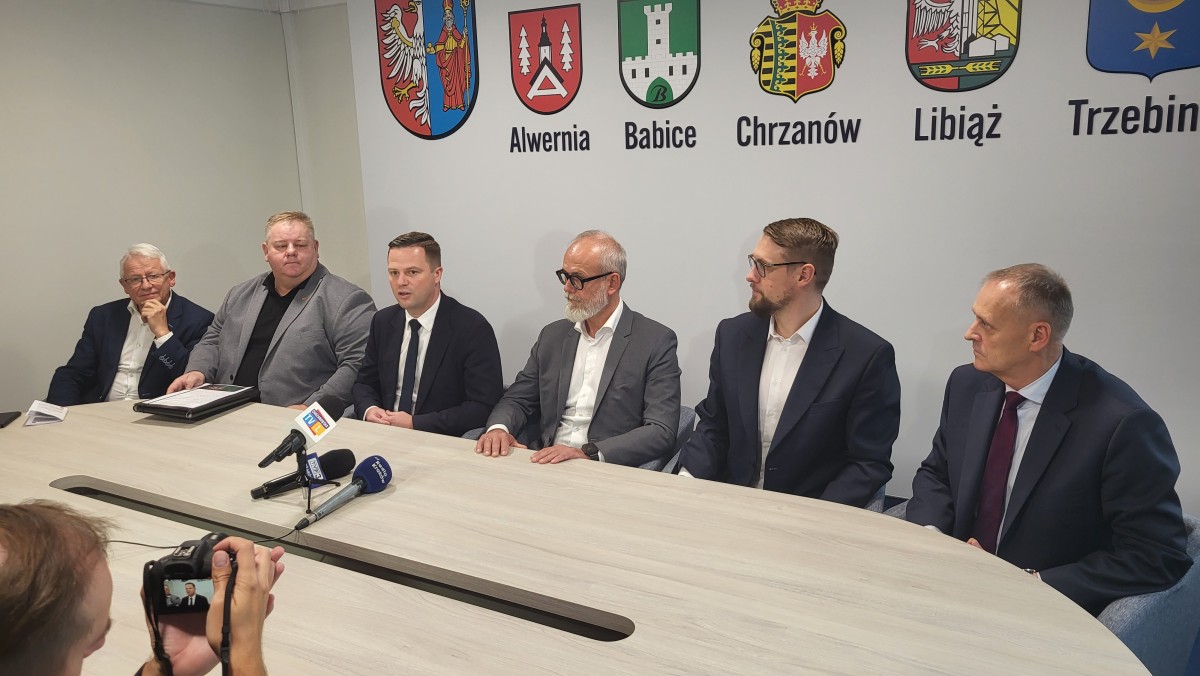 Zdjęcie pięciu mężczyzn siedzących za stołem. Przed nimi trzy mikrofony.