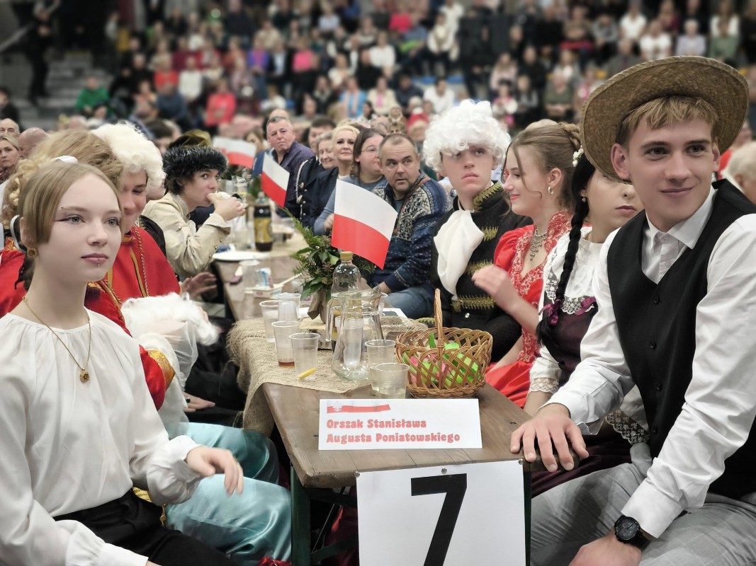 Młodzież przy stole biesiadnym. Przy nich flagi RP