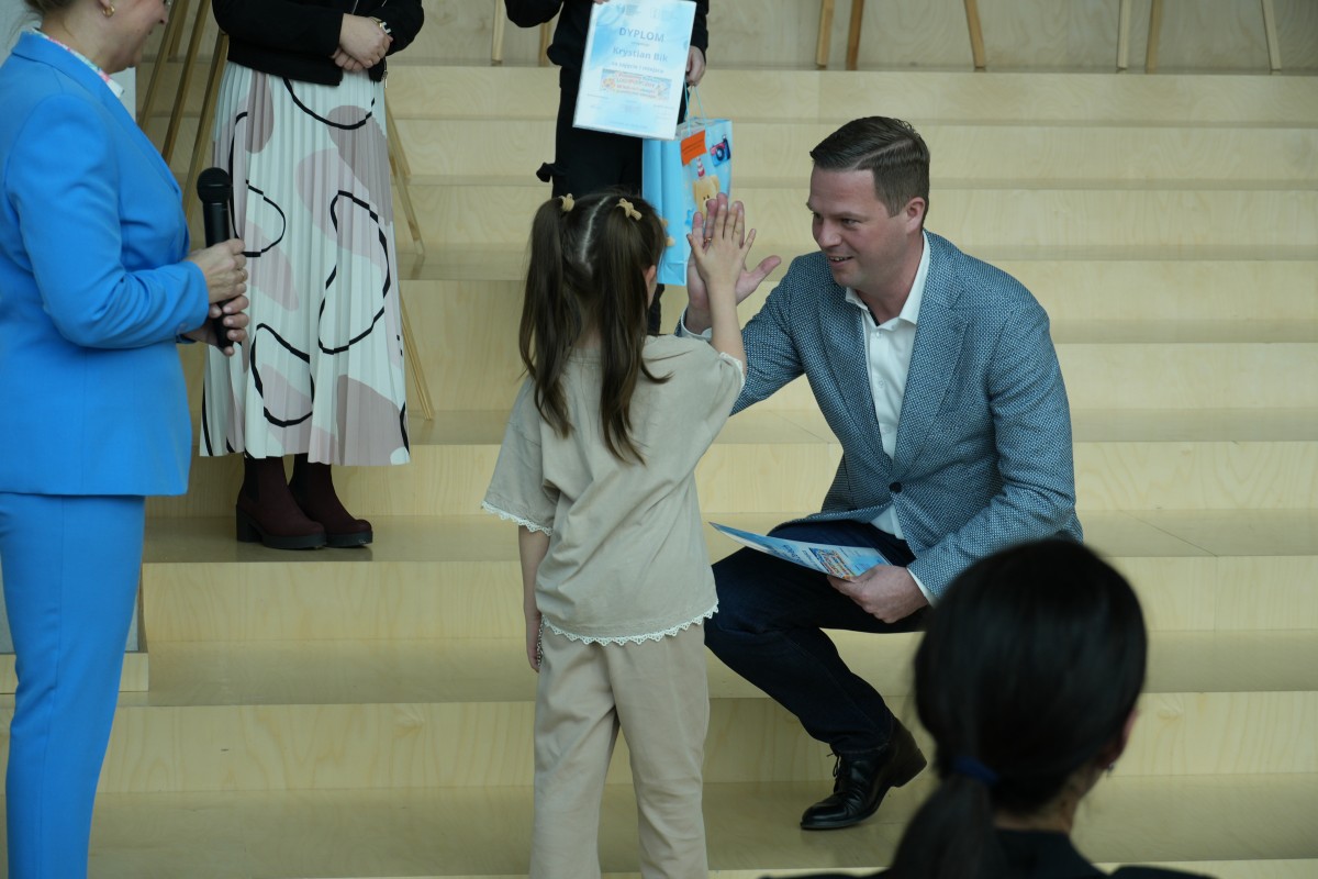 Zdjęcie starosty wręczającej dziewczyne dyplom oraz torbę z nagrodami.