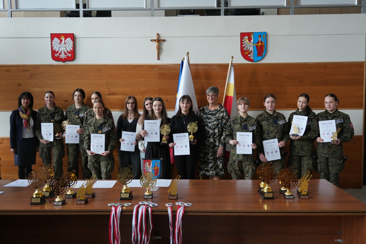 Grupa kilkunastu uczniów pozuje do zdjęcia z dwiema paniami. Uczniowe trzymają dyplomy oraz statuetki.