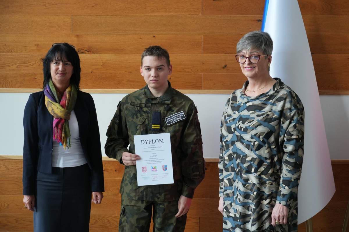 Uczeń pozuje do zdjęcia z dwiema paniami. Uczeń trzyma dyplom.