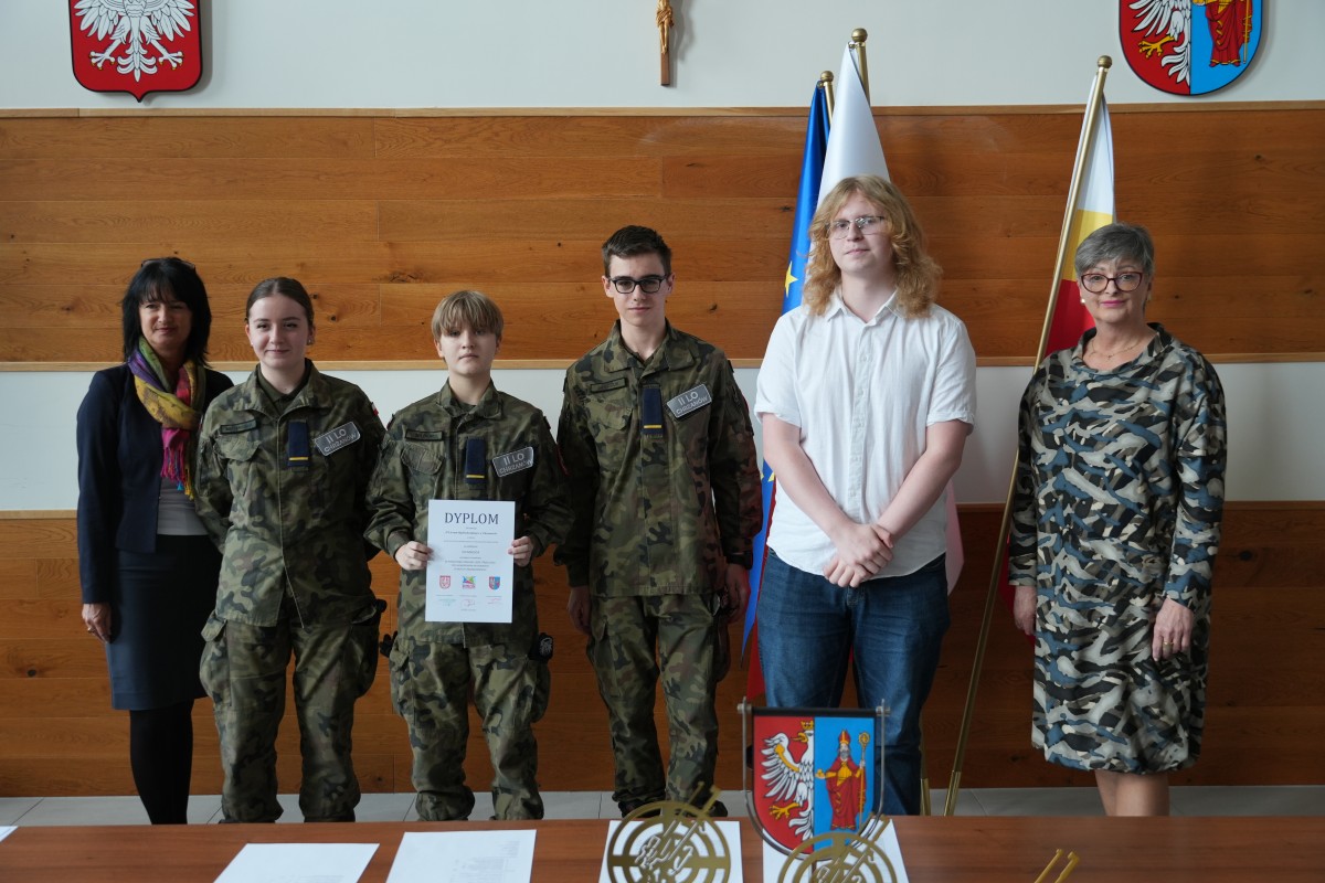 Grupa kilku uczniów pozuje do zdjęcia z dwiema paniami. Uczniowe trzymają dyplomy.