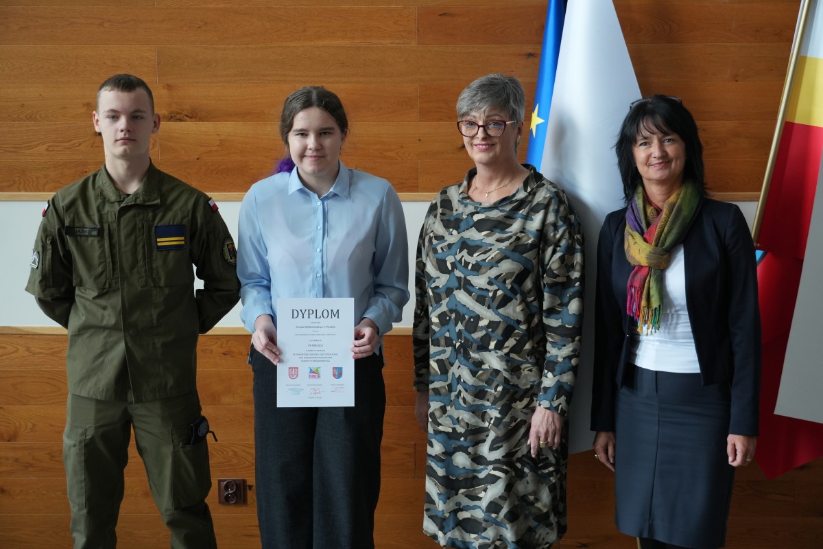 Grupa kilku uczniów pozuje do zdjęcia z dwiema paniami. Uczniowe trzymają dyplomy.