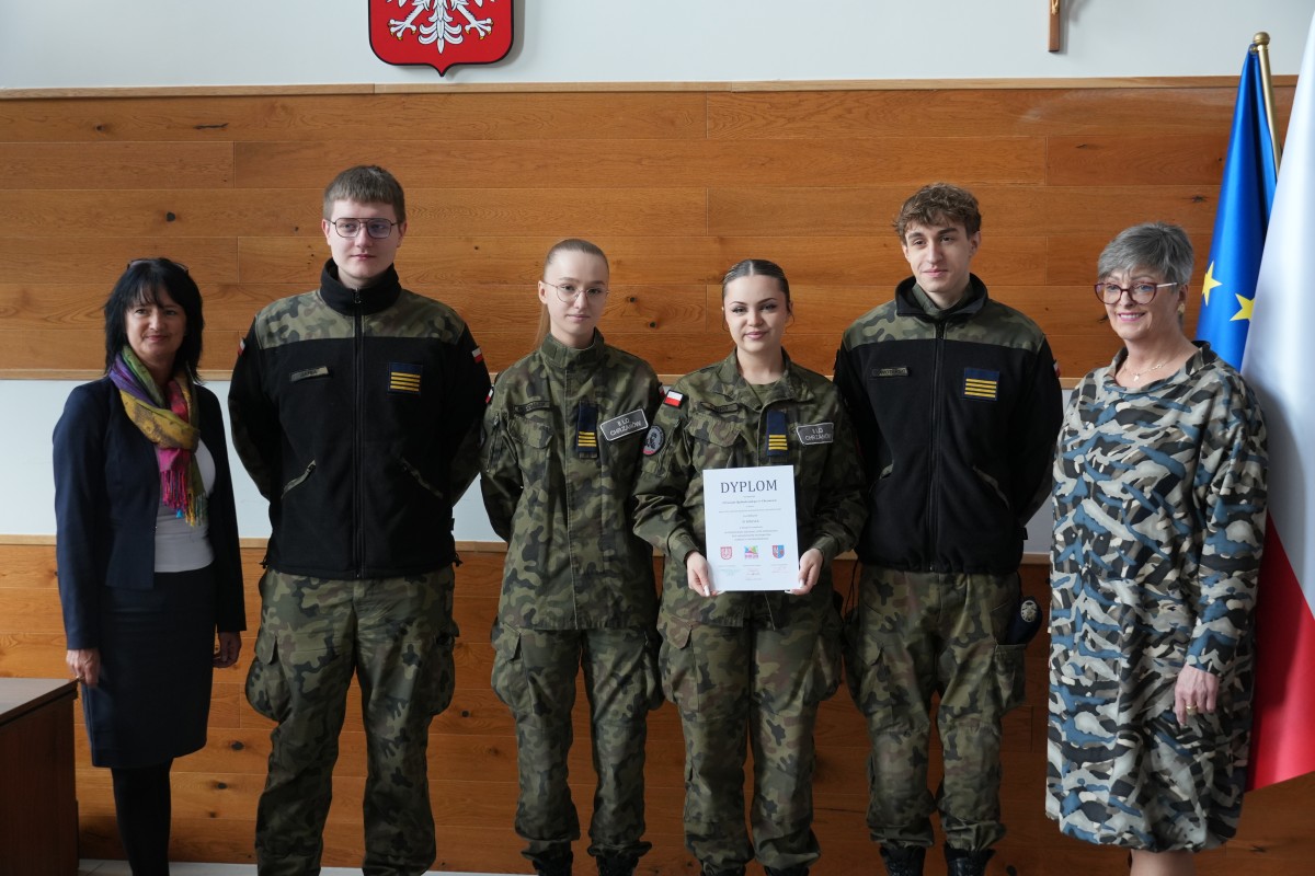 Grupa kilku uczniów pozuje do zdjęcia z dwiema paniami. Uczniowe trzymają dyplomy.