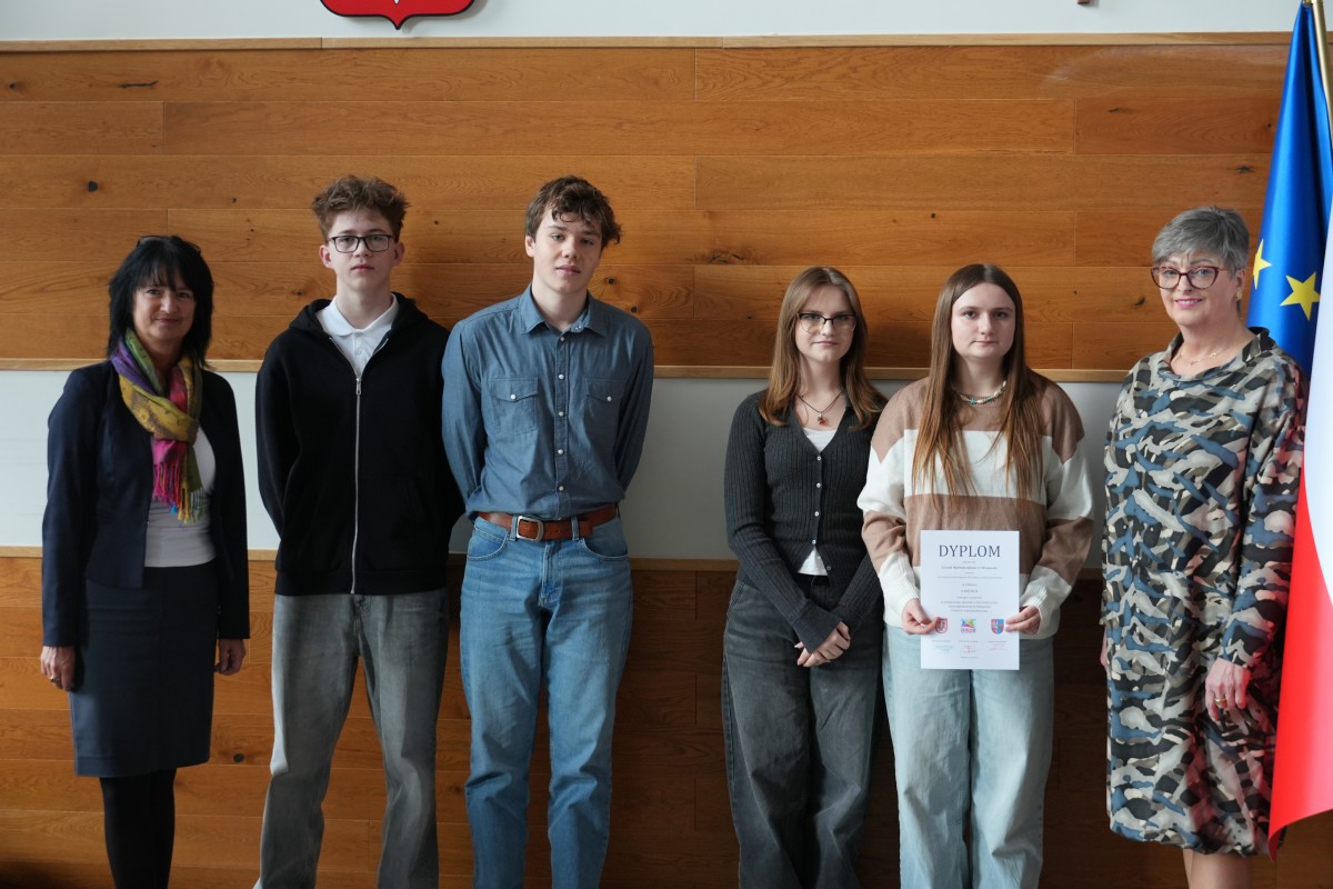 Grupa kilku uczniów pozuje do zdjęcia z dwiema paniami. Uczniowe trzymają dyplomy.