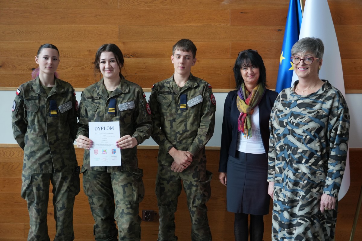 Grupa kilku uczniów pozuje do zdjęcia z dwiema paniami. Uczniowe trzymają dyplomy.