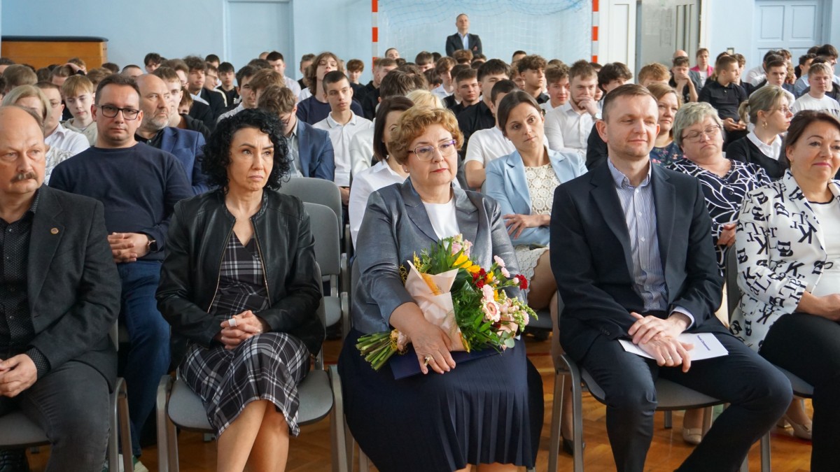 Zdjęcie nauczycieli, uczniów i gości siedzących na hali sportowej podczas uroczystości.