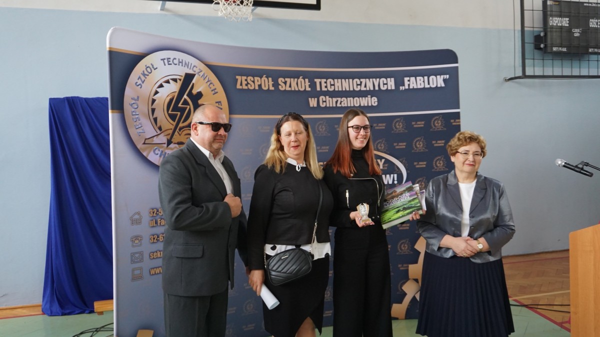 Wspólne zdjęcie dyrektro szkoły, uczennicy i rodziców. W tle ścianka z nazwą szkoły.