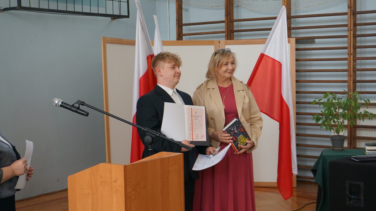 Wspólne zdjęcie ucznia trzymającego świadectwo z czerownym paskiem i dorosłej kobiety.