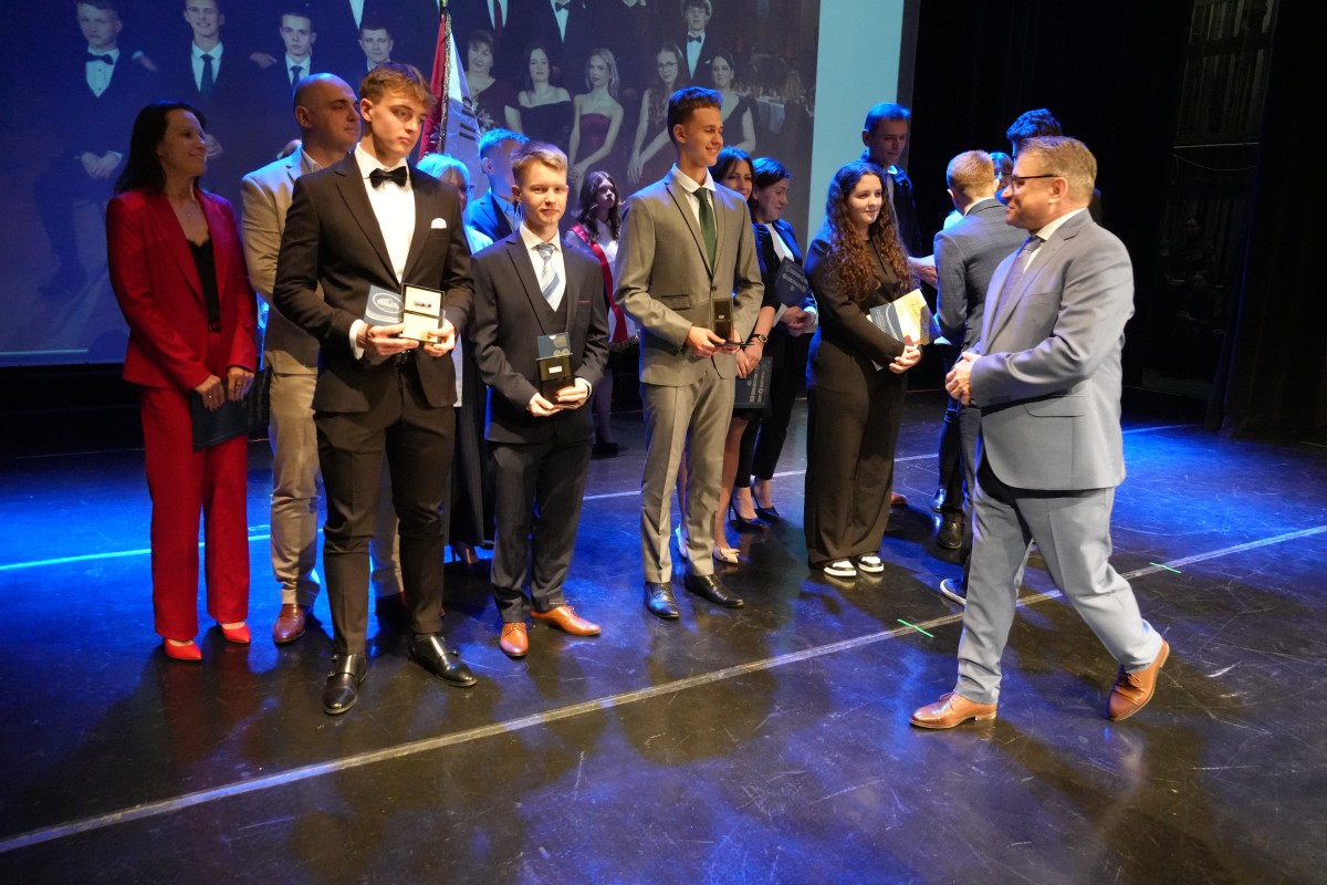 Dyrektor szkoły wręcza uczniom wyróżnienia na scenie.