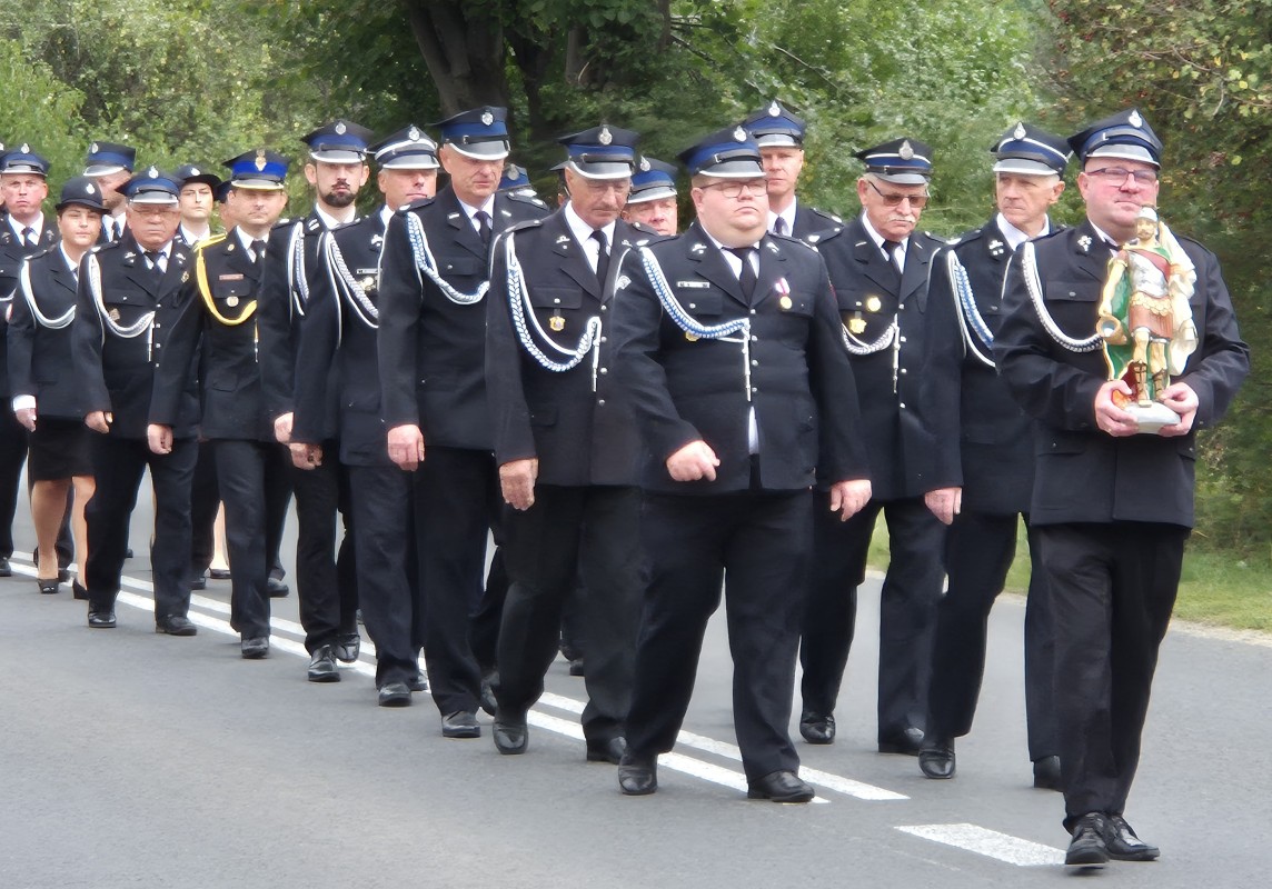 Strażacy idą drogą z kościoła w stronę remizy