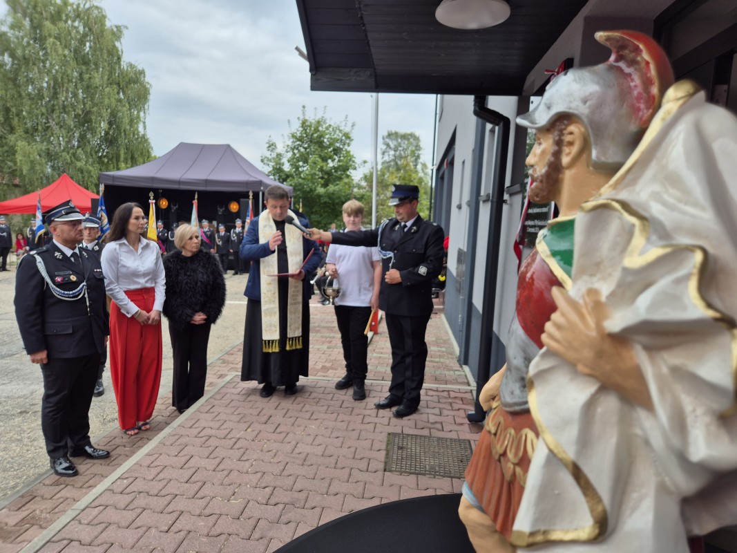 Poświęcenie pamiątkowej tablicy. Stoi ksiądz, sołtys, radna i burmistrz Trzebini wraz z ministrantem i strażakiem
