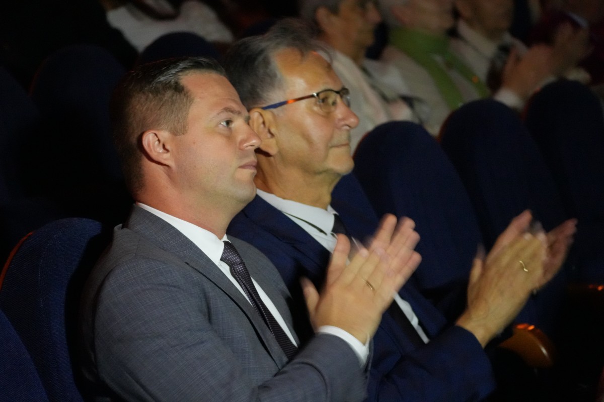 Zdjęcie dwóch siedzących mężczyzn w garniturach, którzy biją brawo.