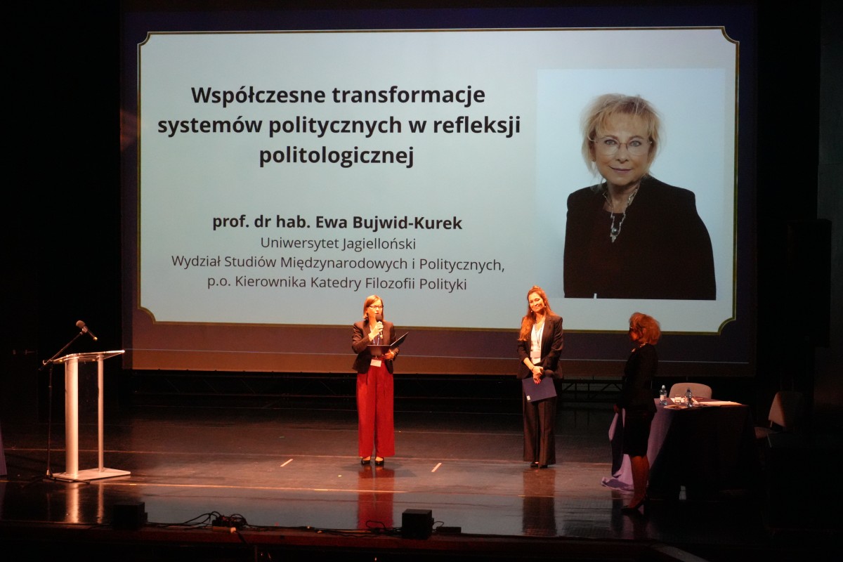 Zdjęcie trzech kobiet stojących na środku sceny. W tle grafika tytułowa wystąpienia za zdjęciem kobiety.