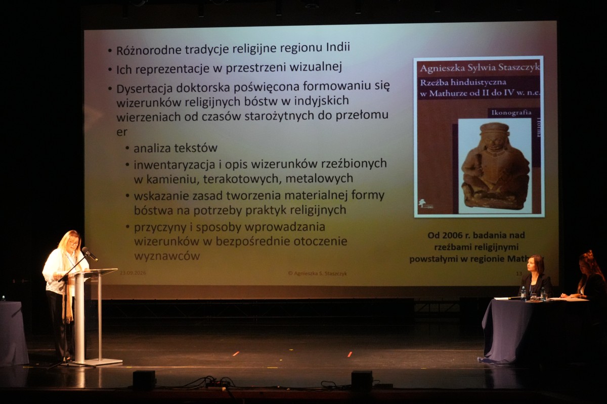 Zdjęcie kobiety przemawiającej zza mównicy. W tle prezentacja.