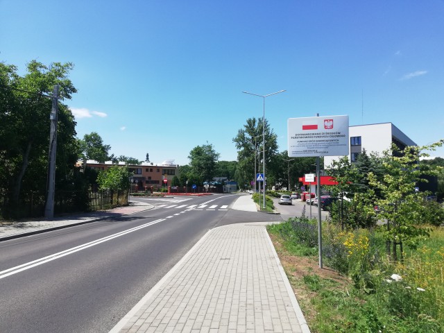 widok na ul krakowskka szary asfalt po prawej chodnik j. szary z kostki w tle drzewa i budynek urzędu po prawej stronie szara tablica informacyjna