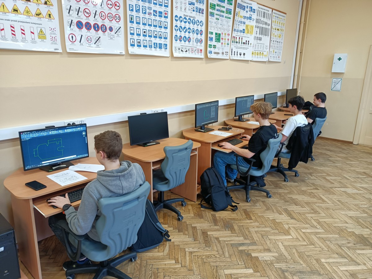 Zdjęcie 4 uczniów, którzy siedzą w fotelach przy stanowiskach komputerowych. Na ekranie każdego z nich widać, że pracują nad tworzeniem i modyfikacją dokumentacji technicznej rysunkowej 2D.