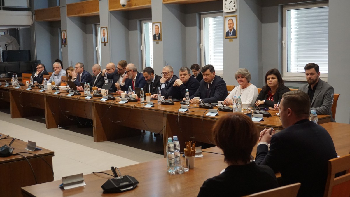 Zdjęcie kilkunastu osób zasiadających przy stołach z jednej strony sali narad w starostwie powiatowym w Chrzanowie. W prawym dolnym rogu zdjęcia widać Starostę i Wicestarostę.