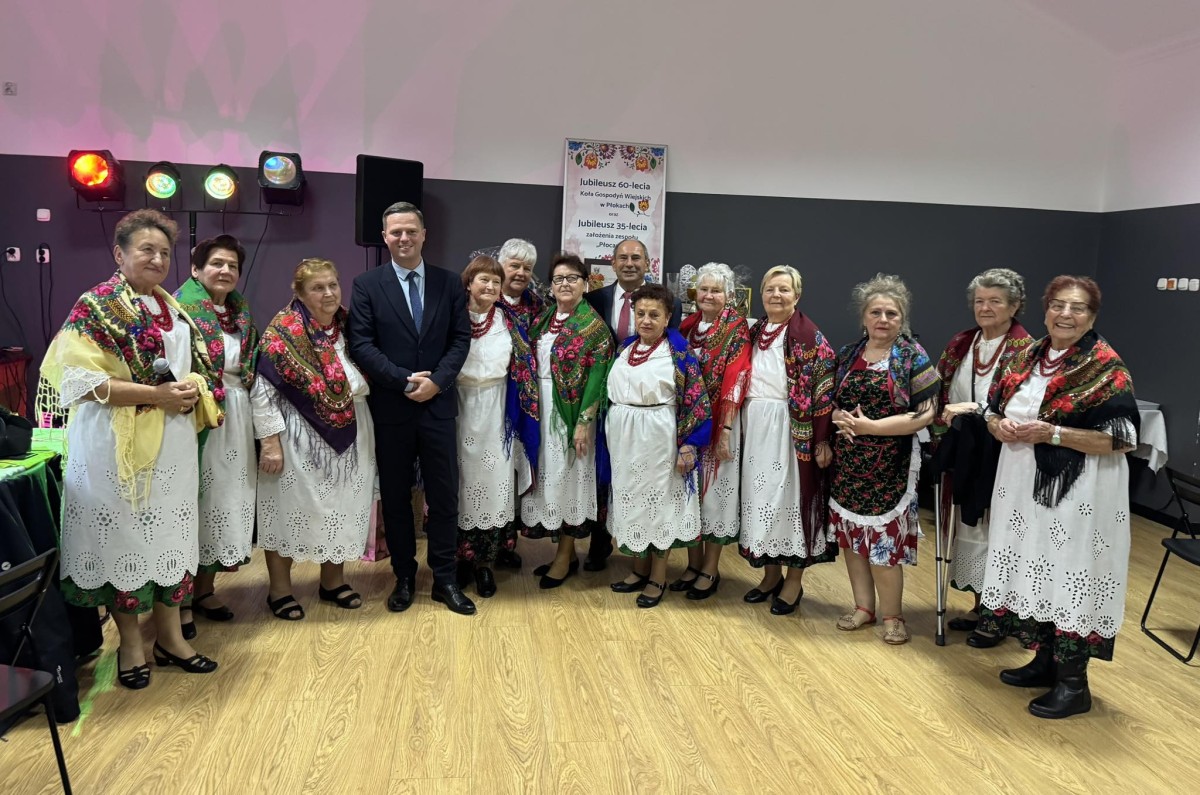 Mężczyzna w garniturze, w otoczeniu kobiet w strojach regionalnych 