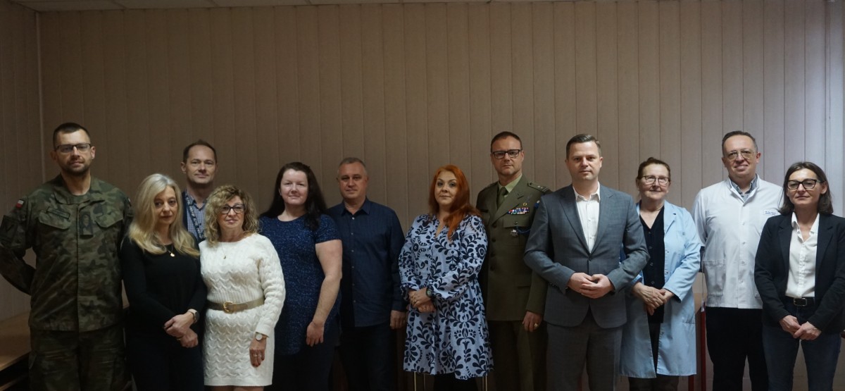 Zdjęcie 12 osób stojących obok siebie. Na zdjeciu kobiety i mężczyźni. Niektórzy z nich w munudrach, kitlach i garniturach. 
