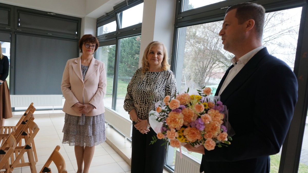 Mężczyzna z bukietem kwiatów, obok dwie kobiety. Uśmiechają się 
