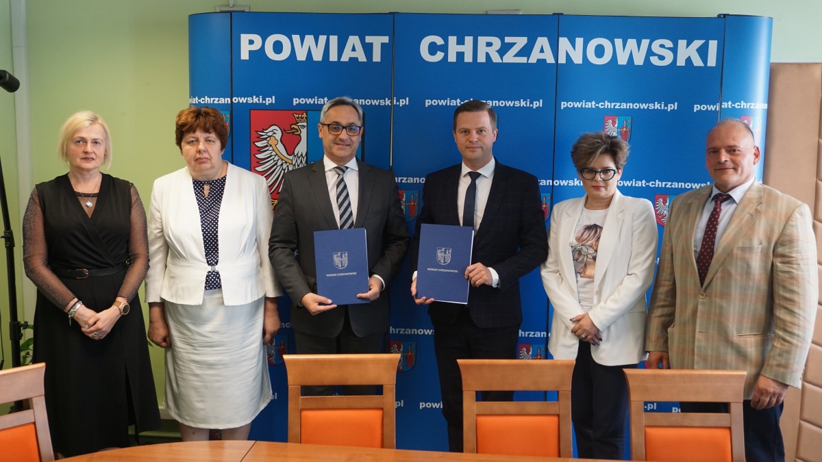 dyr ops, skarbnik libiaża, wiceburmistrz Libiąża, wicestarosta, skarbnik powiatu, cżł. zarządu powiatu stoja przed niebieską ścianką z herbami powiatu chrzanowskiego. WST i Wiceburmistrz prezentują teczki z podpisaną umową 