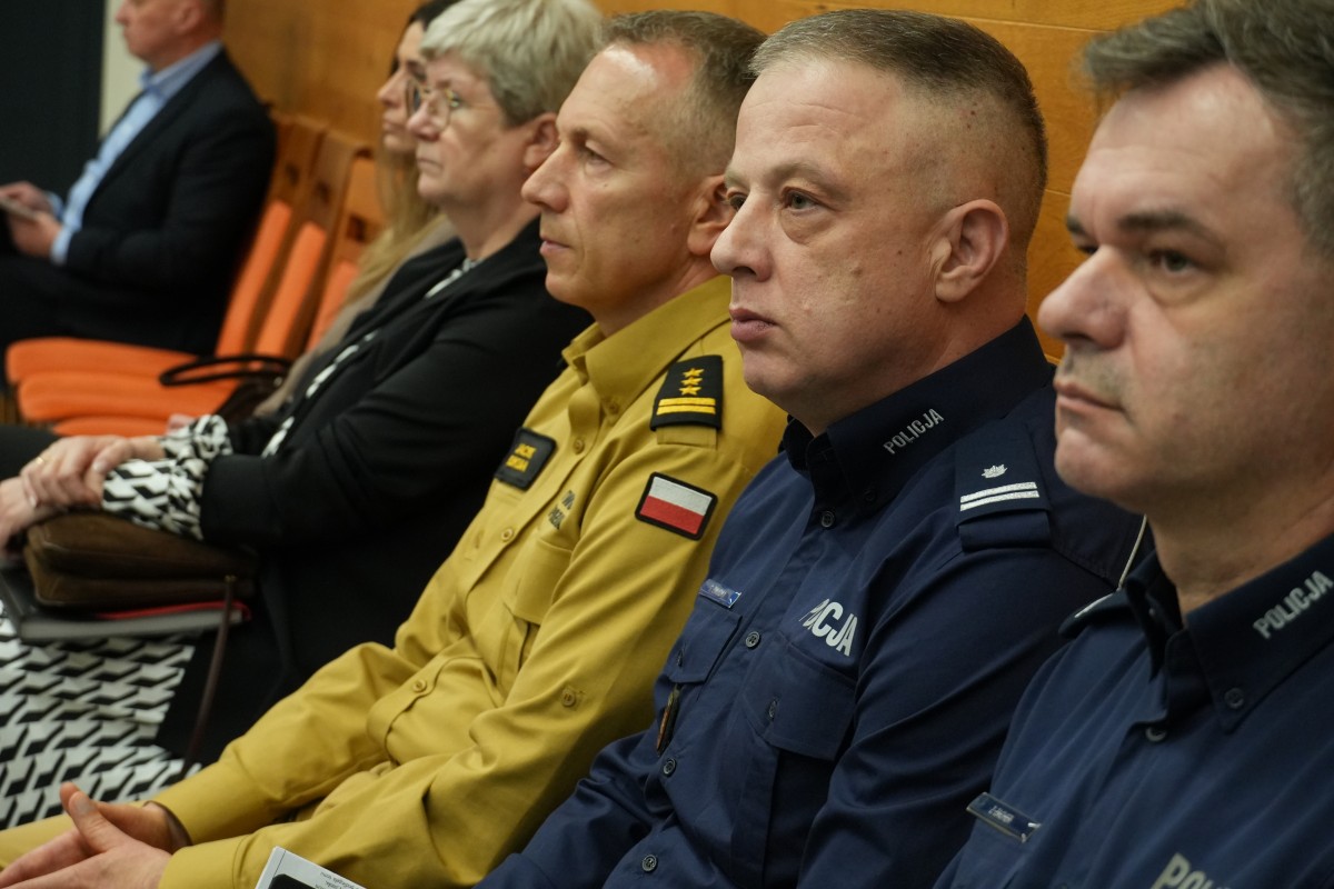 Dwóch policjantów, strażak, dwie kobiety. Wszyscy w pozycji siedzącej 