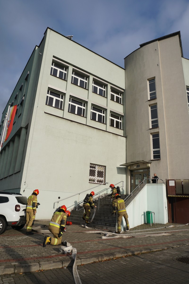 Strażacy rozwijają węże pożarnicze przed budynkiem starostwa 