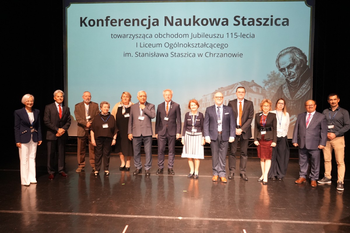 Zdjęcie kilkunastu osób na scenie. W tle rzutnik wyświetlający plansze związaną z wydarzeniem.