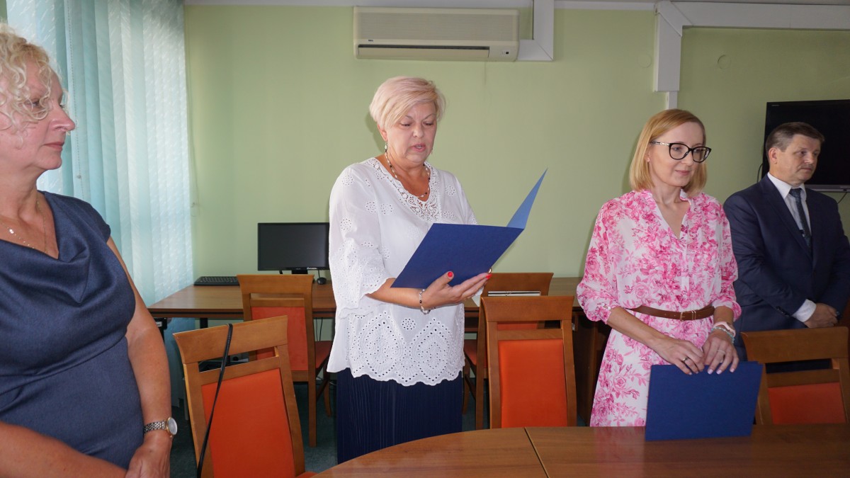 Kobieta trzyma w ręku okładkę, czyta. Obok dwie inne kobiety i mężczyzna w garniturze 