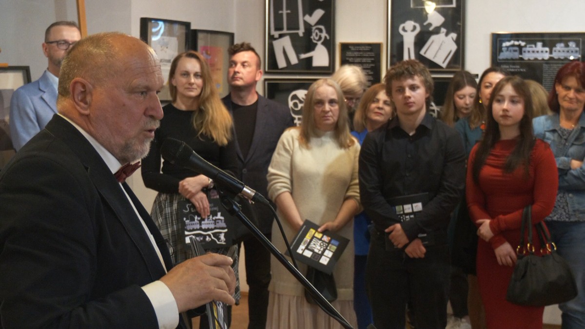 Do mikrofonu przemawia mężczyzna, w tle inne osoby