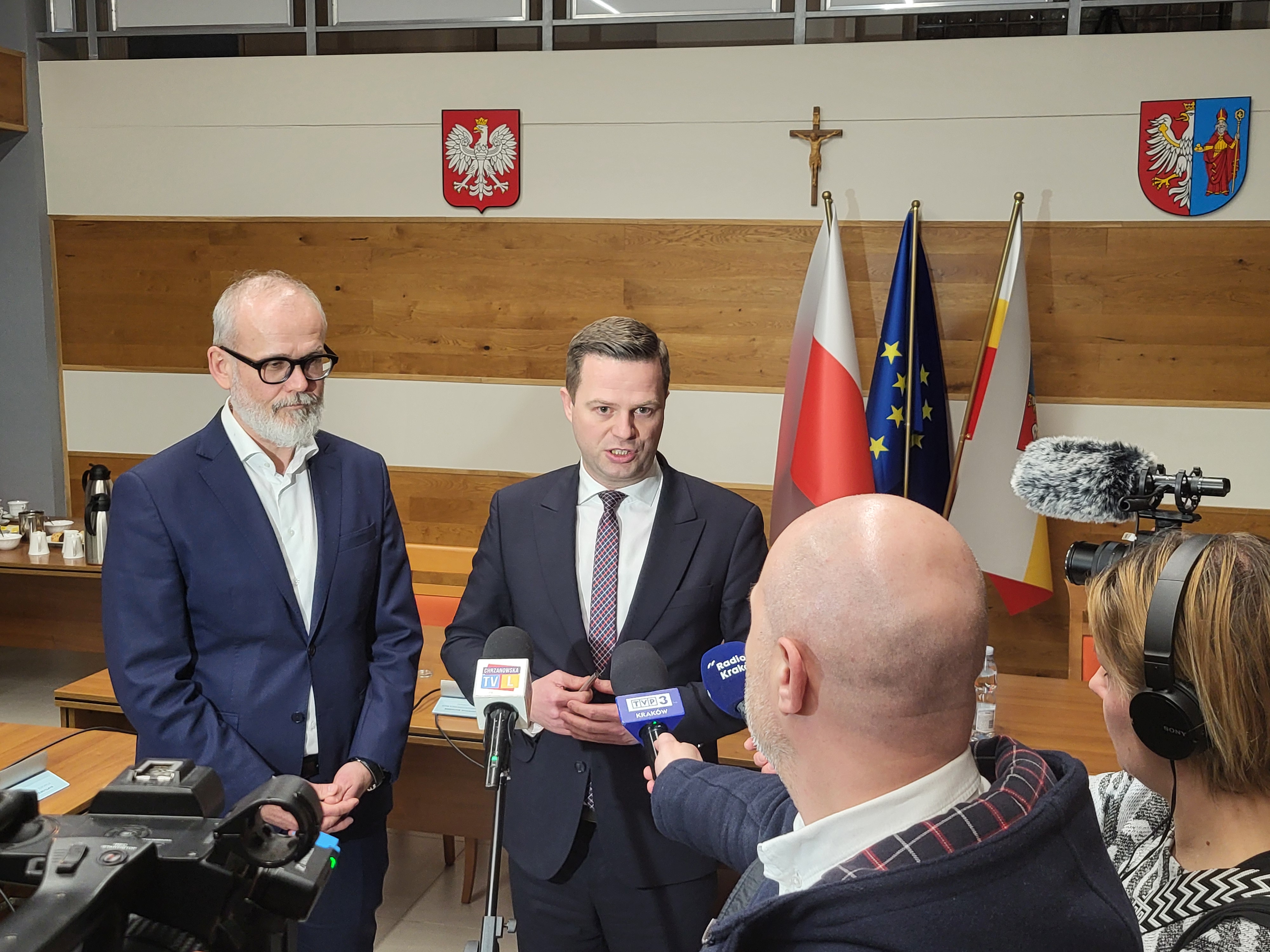Starosta oraz Prezes Tauron stojący obok siebie na sali konferencyjnej. Przed nimi dziennikarze z mikrofonami i kamerami. 
