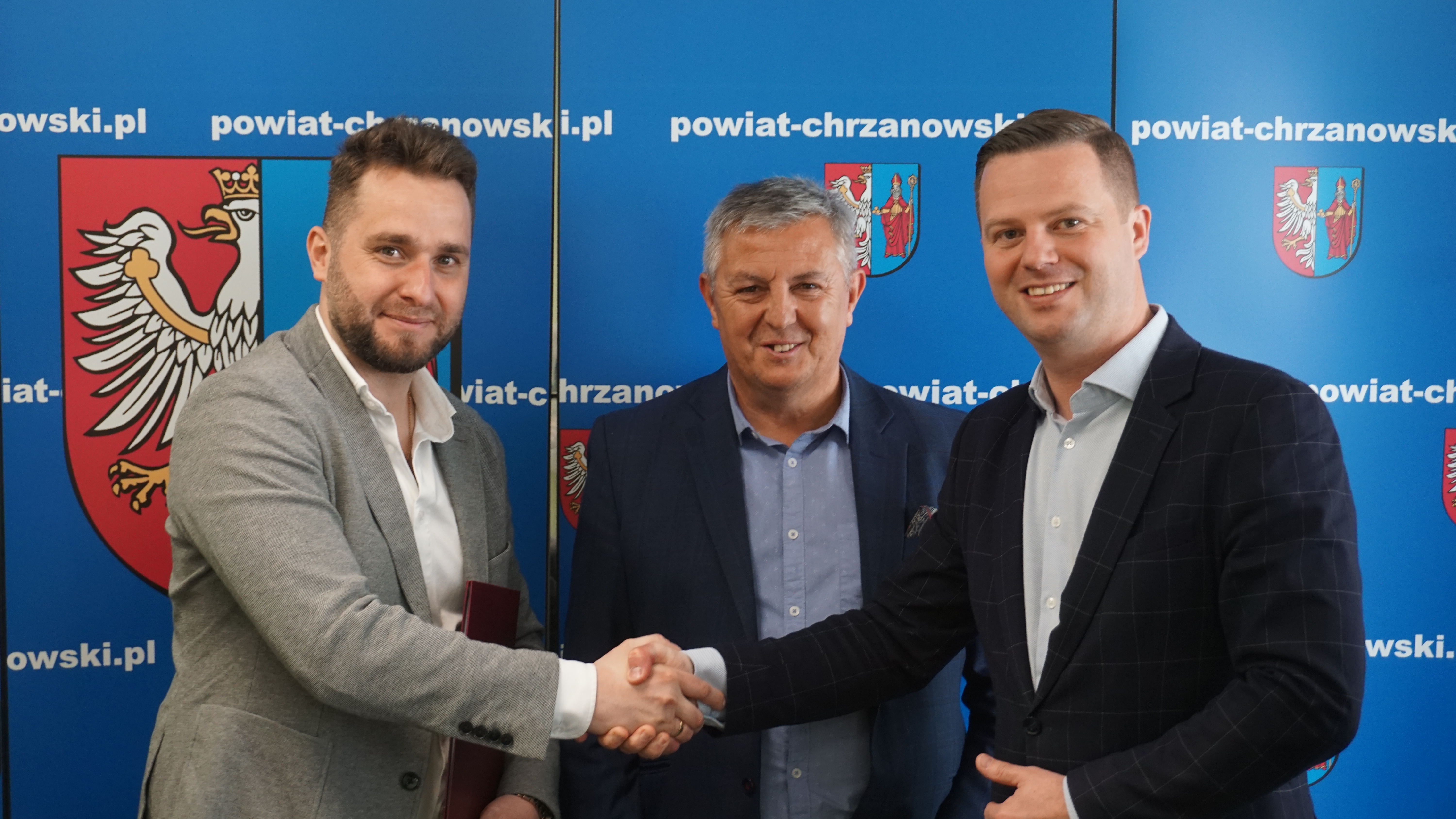 Zdjęcie 3 męzczyzn. Dwójka z nich ściska sobie dłonie. 