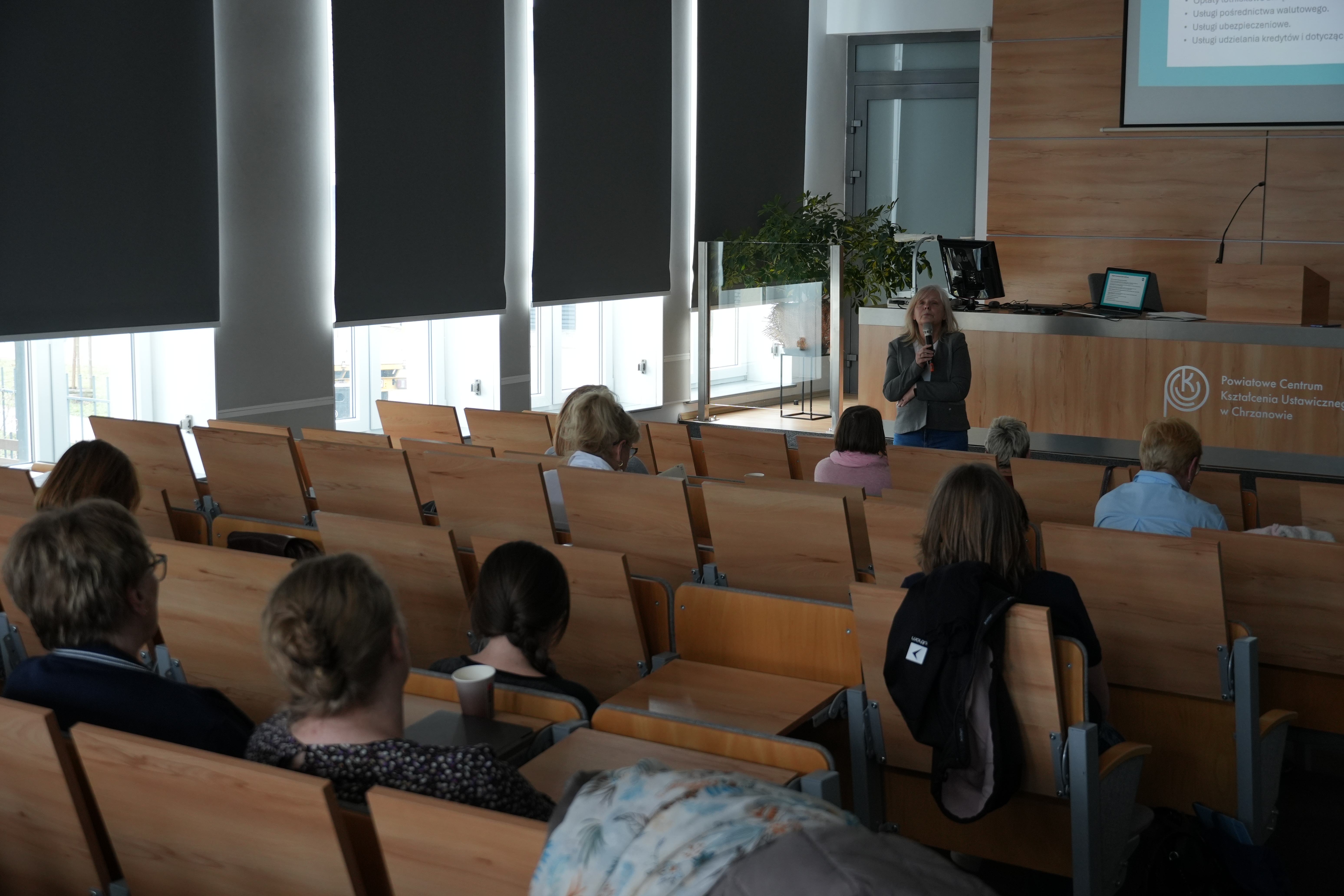 Zdjęcie sali wykładowej z kilkudziesięcioma osobami. Jedna osoba stoi przy na środku sali i prowadzi szkolenie, reszta osób siedzi.